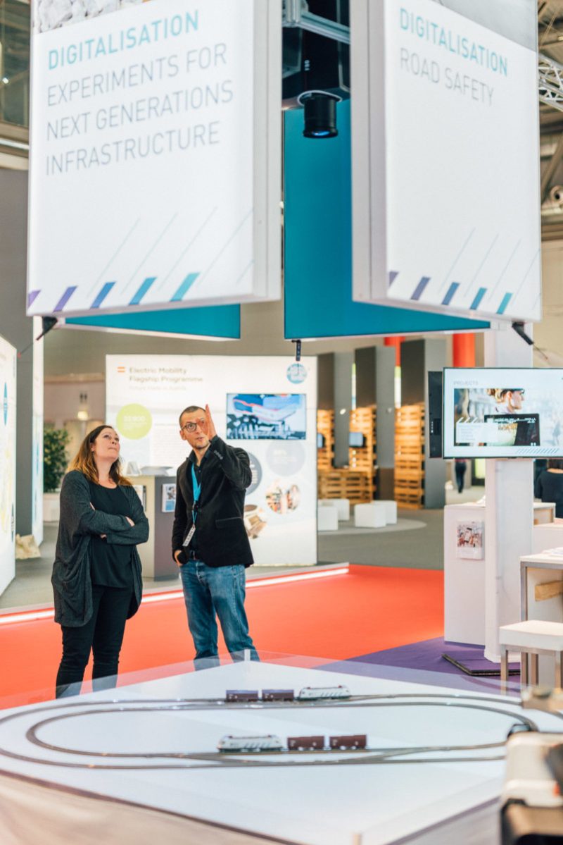 Besucherin und Guide an der projizierten Modelleisenbahn am AIT-Stand, darüber Banner zur Digitalisierung
