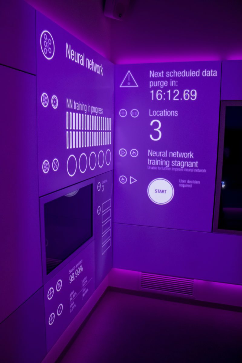 Purple-lit wall projection showing neural network training progress and a start button