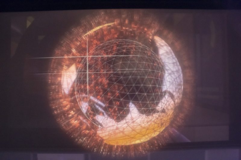 Close-up of a wireframe sphere with glowing orange particles on a display in the training room