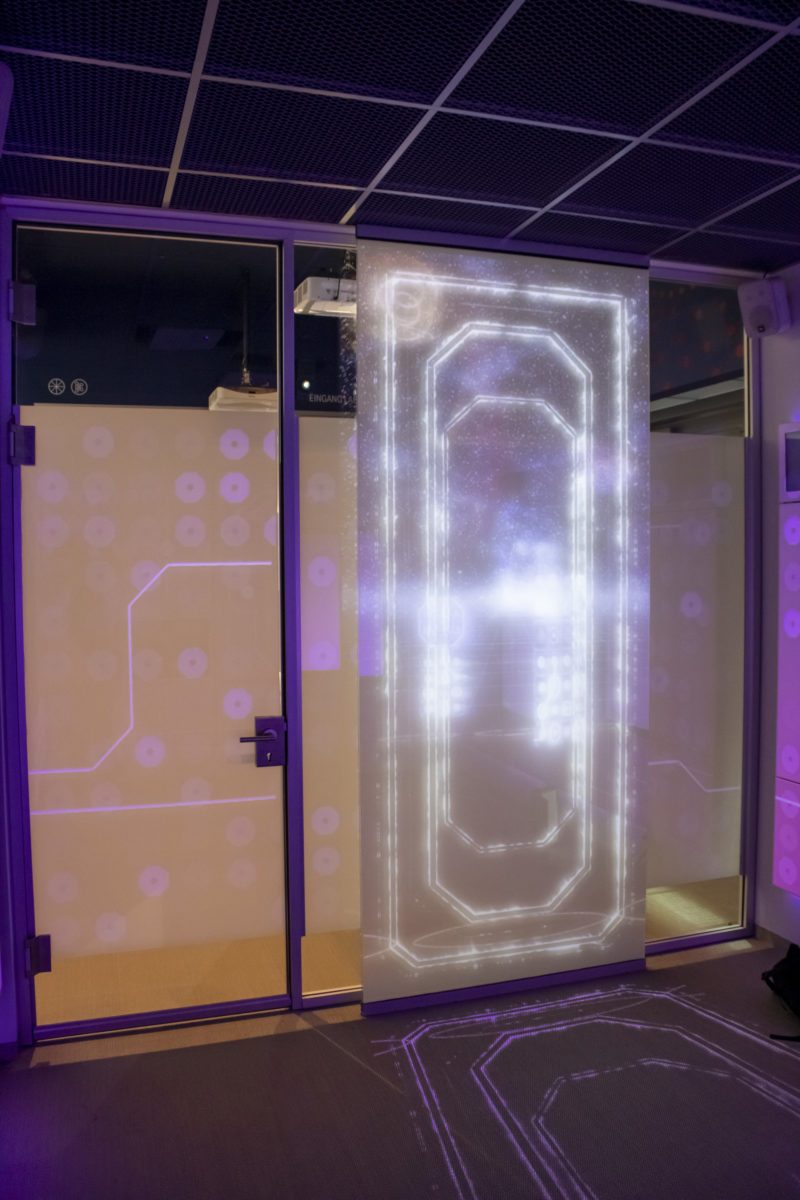 Glass entrance with circuit-board graphics and a glowing projection on a translucent panel