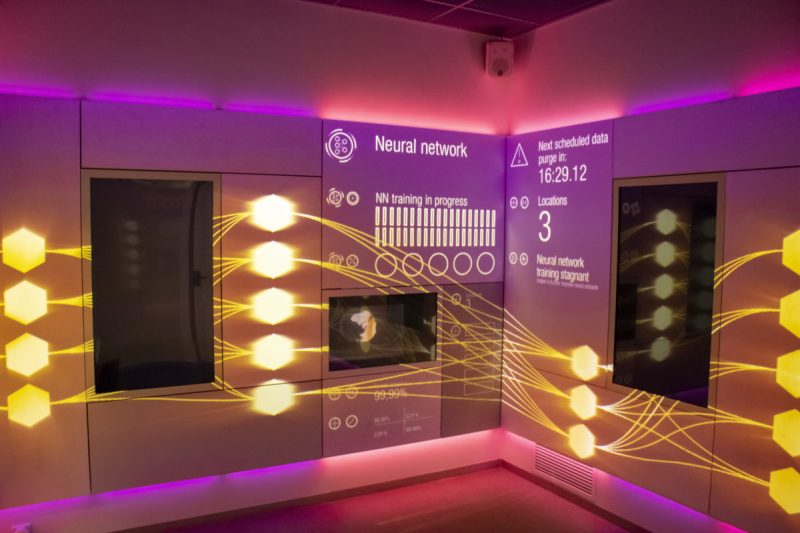 Raumecke mit projiziertem neuronalem Netz aus leuchtenden Sechsecken und Statusanzeigen im BMW Digital Discovery Space