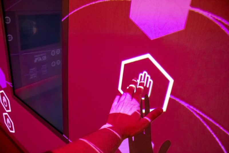 Hand activating a projected hexagon node marked with a hand icon on the wall