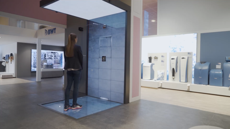 Besucherin in der virtuellen Dusche mit Displays in Decke und Boden, daneben BWT-Wasseraufbereitungsgeräte
