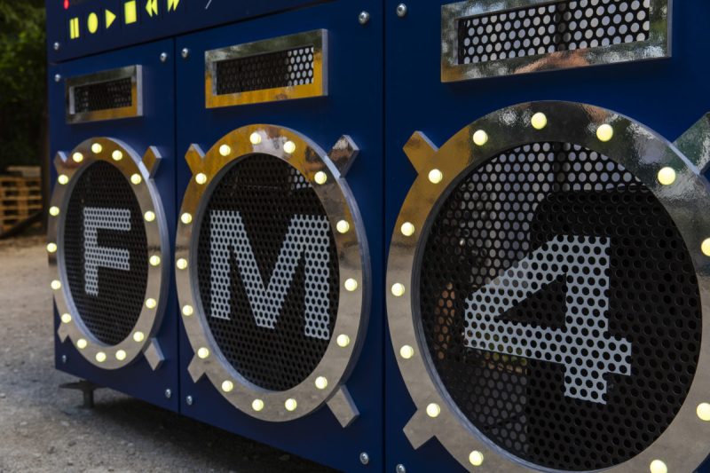 Angled view of the speaker front spelling F, M and 4 inside chrome rings lit with LEDs