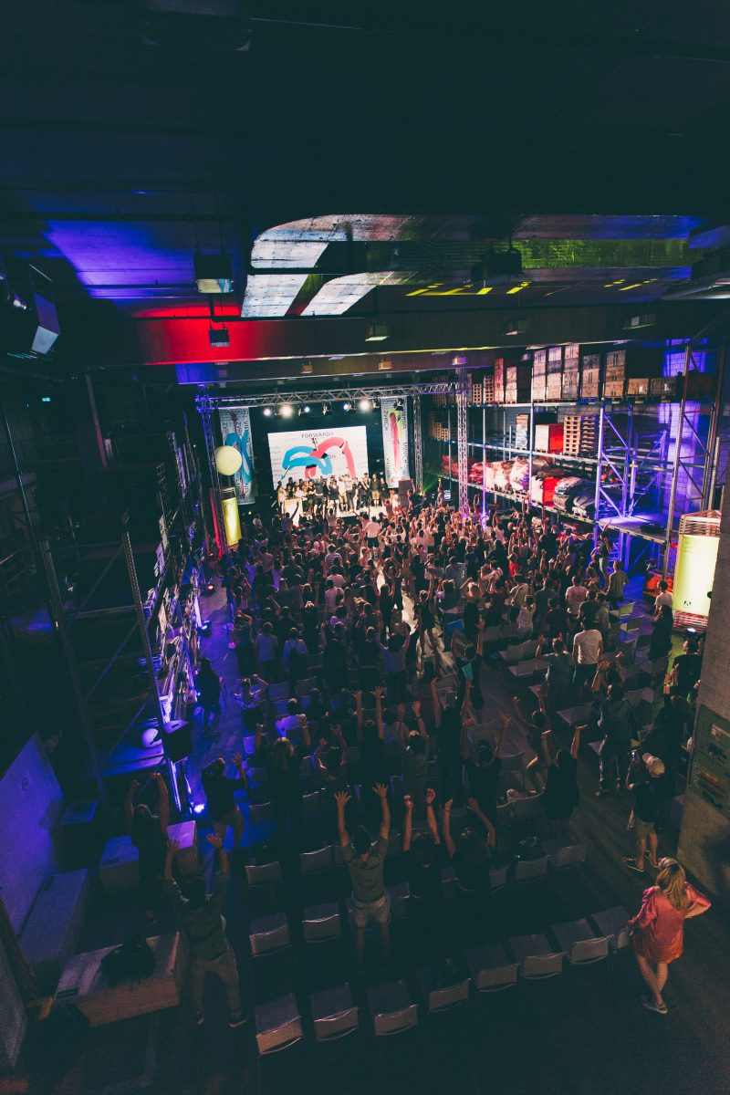 Forward Festival Zürich von oben: Publikum mit erhobenen Armen vor der Bühne in einer Lagerhalle