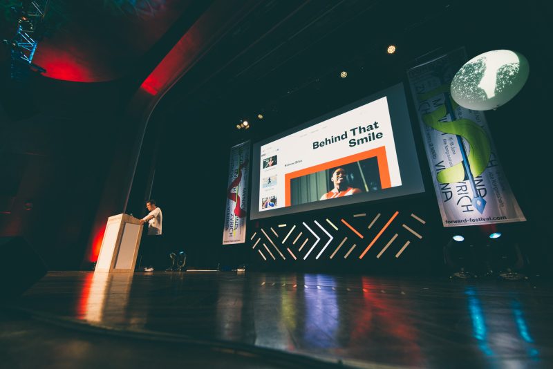 Forward Festival München: Sprecher am Pult vor großem Screen und LED-Stagedesign mit Winkelmuster