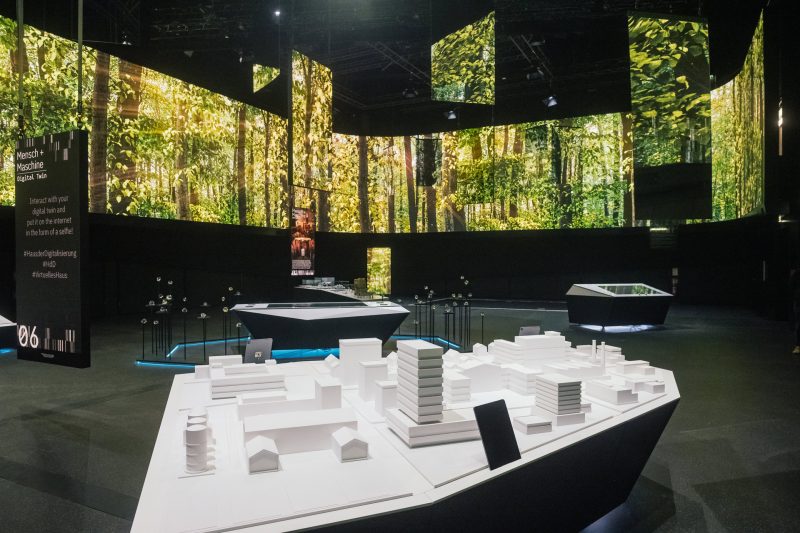 Showroom with a 360° LED wall full of forest imagery and the white 3D city model of the AR station