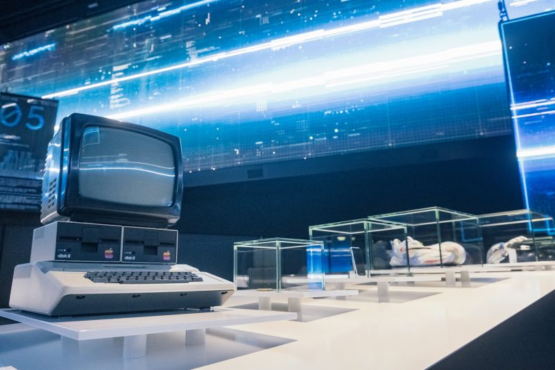 Apple II computer and glass cases of the physical timeline in front of a glowing blue LED wall