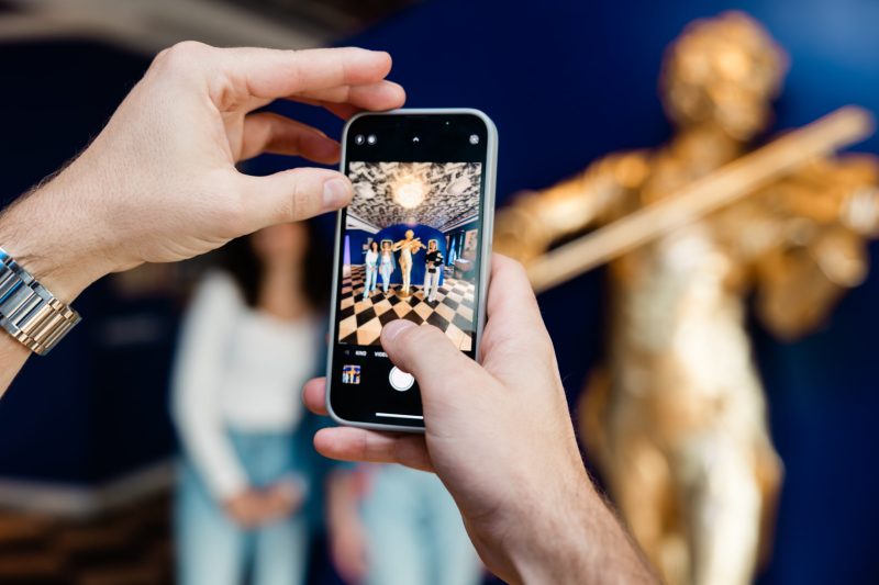 Smartphone photographing visitors next to a golden Strauss statue in the museum