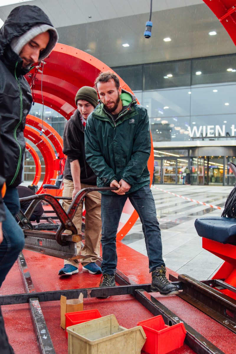 Aufbauteam setzt mit Hebelwerkzeug die Gleise ein, im Hintergrund der Eingang des Wiener Hauptbahnhofs