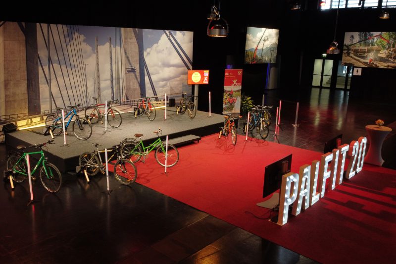 Bühne mit zehn Fahrrädern auf Rollentrainern, Leuchtschrift „PALFIT 20“ und Live-Screen vor dem Spendenradeln