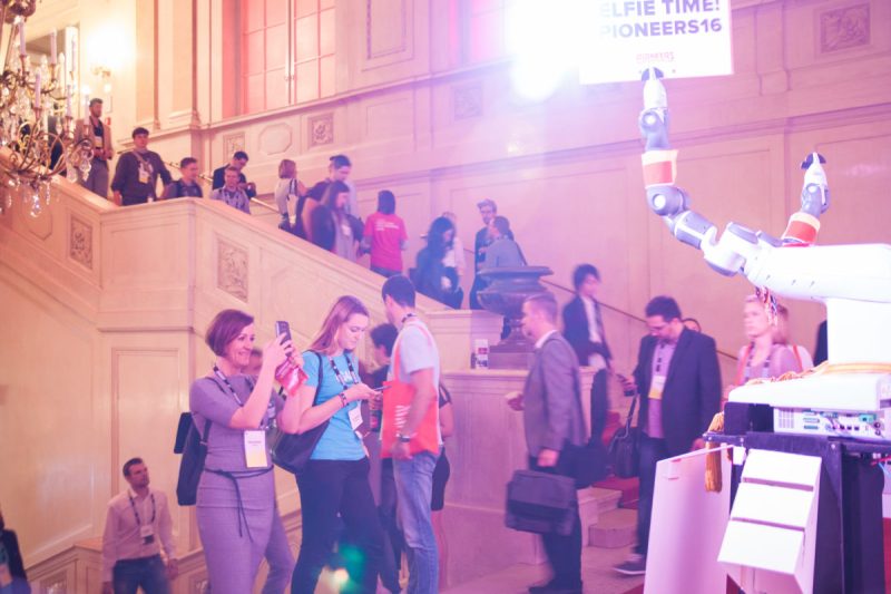 Besucher:innen im Treppenhaus neben einem Roboterarm und dem Schild „Selfie Time! Pioneers16“
