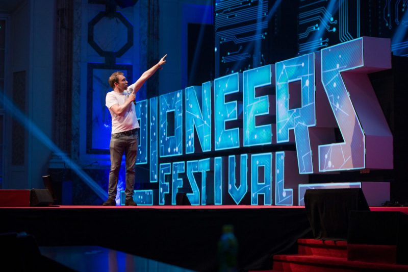 Speaker auf der Bühne vor großen, mit Platinen-Grafik bespielten Pioneers-Festival-Lettern
