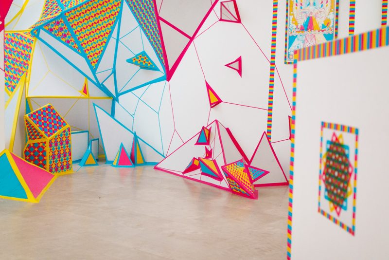 Geometric wall pieces and polyhedra with diamond patterns in magenta, cyan and yellow on white
