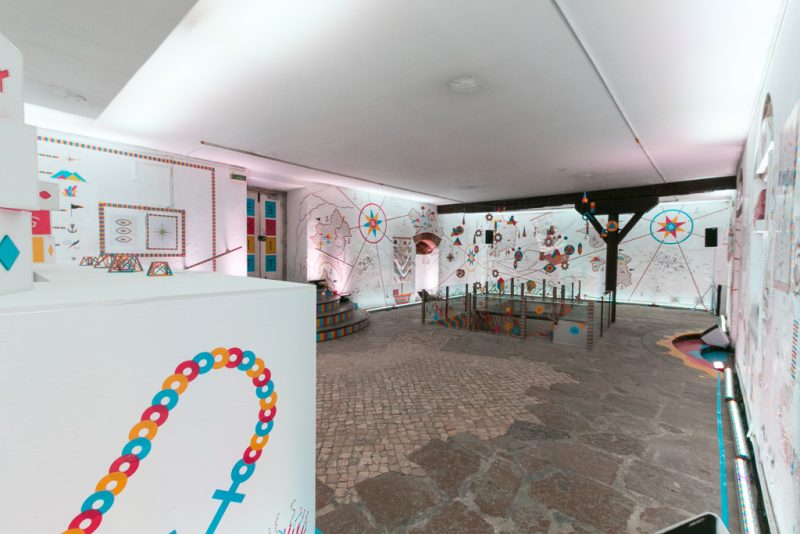 Cascais station: exhibition space with cobblestone floor, painted walls and colourful symbols in daylight