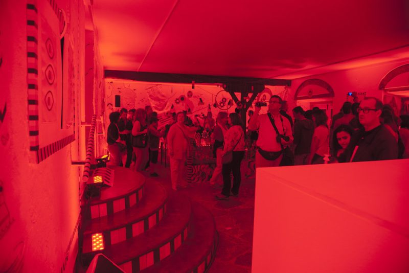 Visitors walk through the Ring Ging Bling exhibition while the whole room is bathed in red light