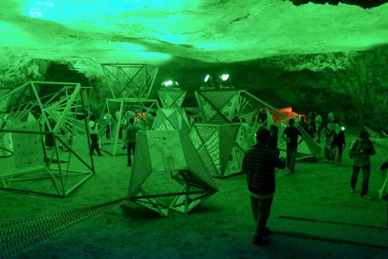 Visitors moving between the sculptures in the cave as everything is bathed in green light