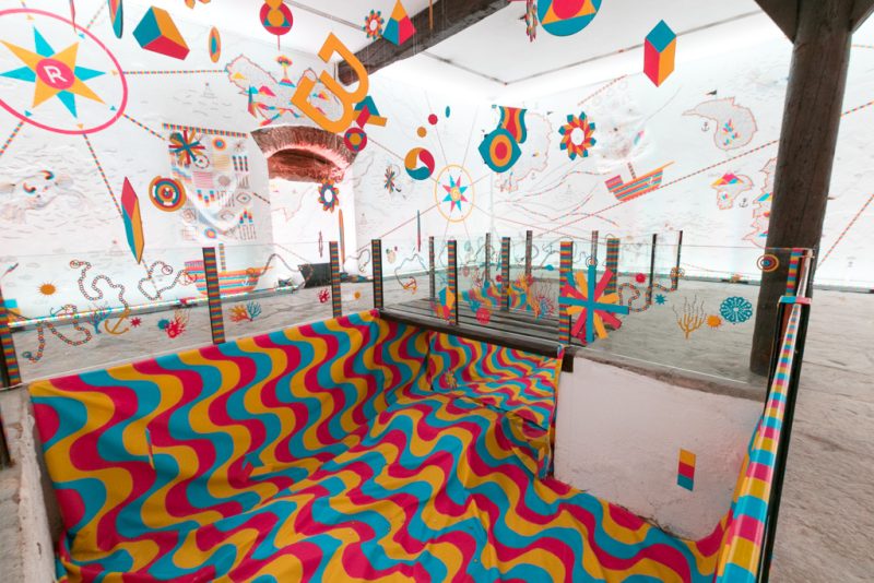 Pit lined with wave-patterned fabric in Cascais, beneath floating letters and geometric shapes