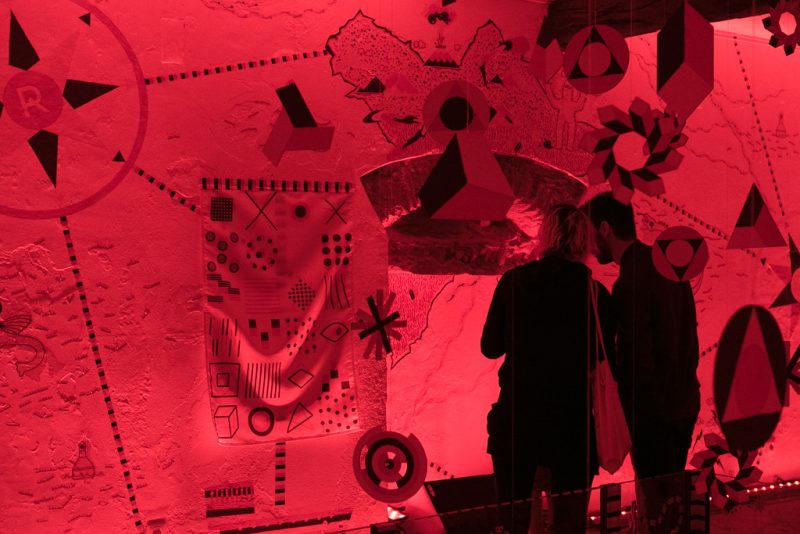 Silhouettes of two visitors in front of a wall map and symbols transformed by the red light