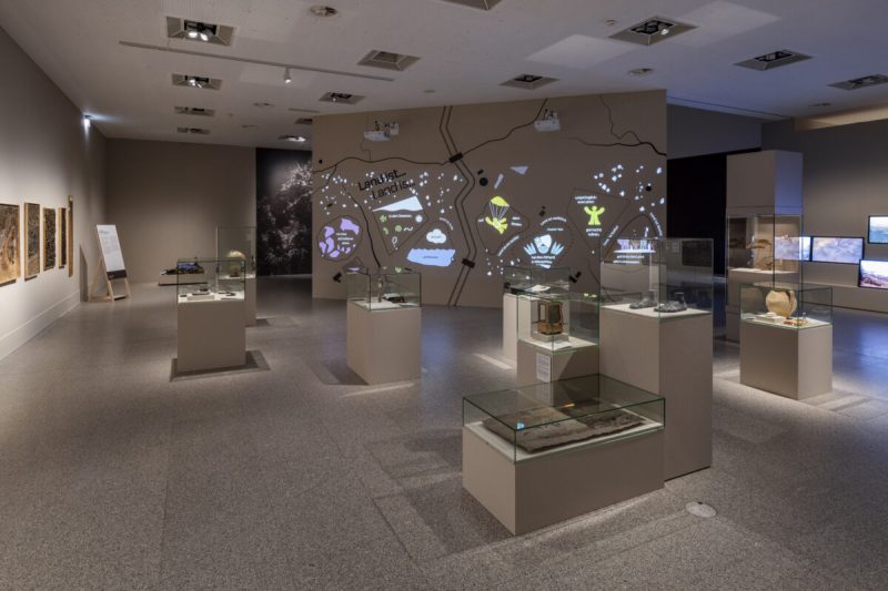 Exhibition hall with display cases and the projected wall graphic “Land ist …” at Bundeskunsthalle Bonn