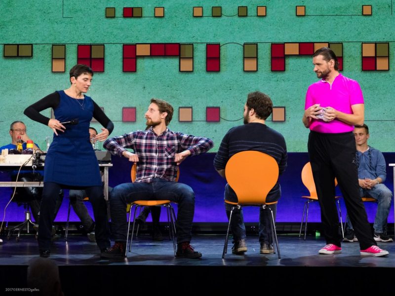 Stage scene with an audience experiment on chairs in front of a projected grid of coloured squares
