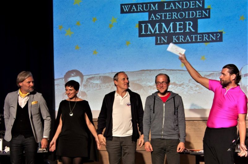 Five cast members at the final applause beneath the projection Warum landen Asteroiden immer in Kratern