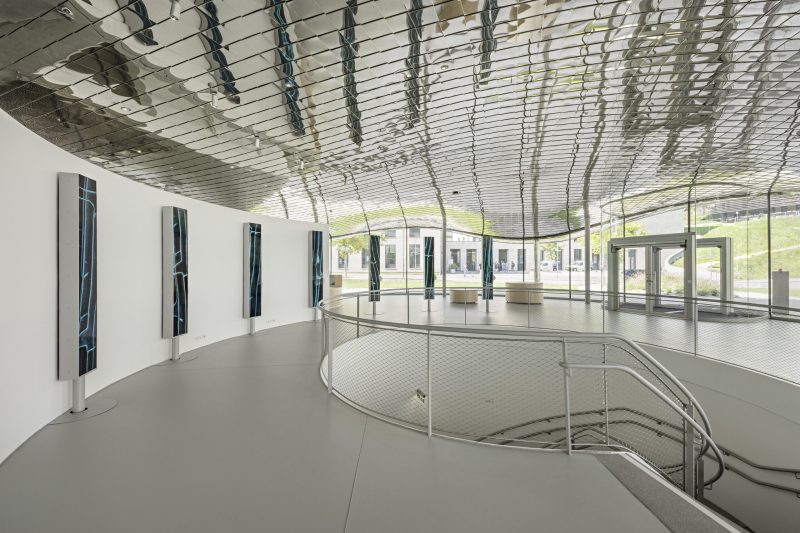 Foyer gallery with display pillars along the curved wall and stairs down to the lower-level exhibition
