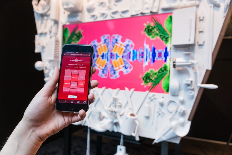Smartphone mit der Heimatgenerator-Webapp und Begriffen wie Äppelwoi, davor die Kuckucksuhr mit Bildcollage