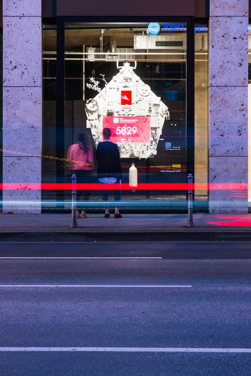 Passers-by at the Vitra shop window with the Heimatgenerator, a white cuckoo clock with a red screen