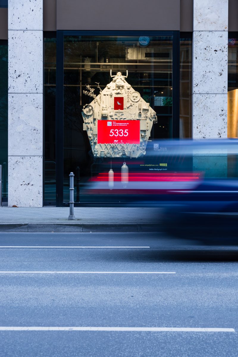 Heimatgenerator im Schaufenster mit Heimatcode am Bildschirm, davor fährt ein Auto vorbei
