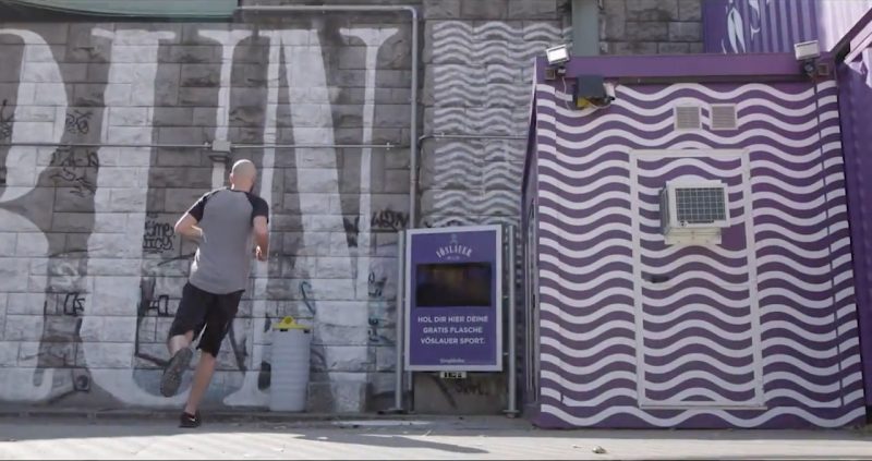 Videostill: Läufer vor der „RUN“-Mauer und dem Screen „Hol dir hier deine Gratis Flasche Vöslauer Sport“